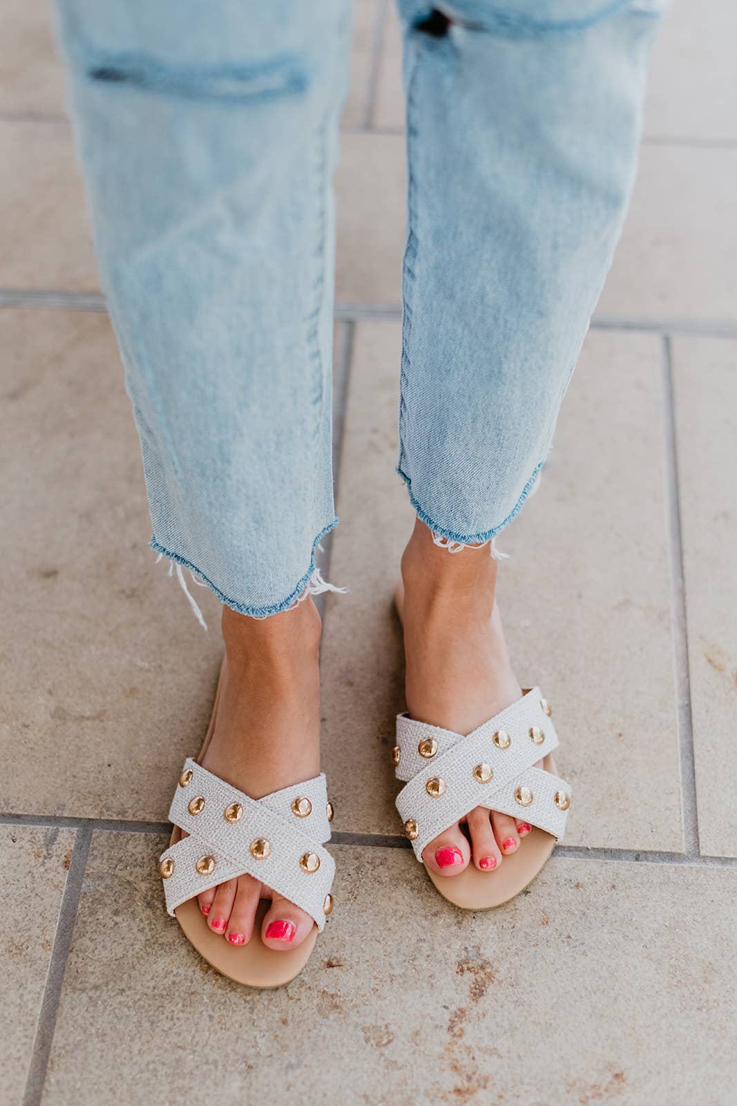 White sandals with gold accents worn with light blue jeans on a tiled floor.