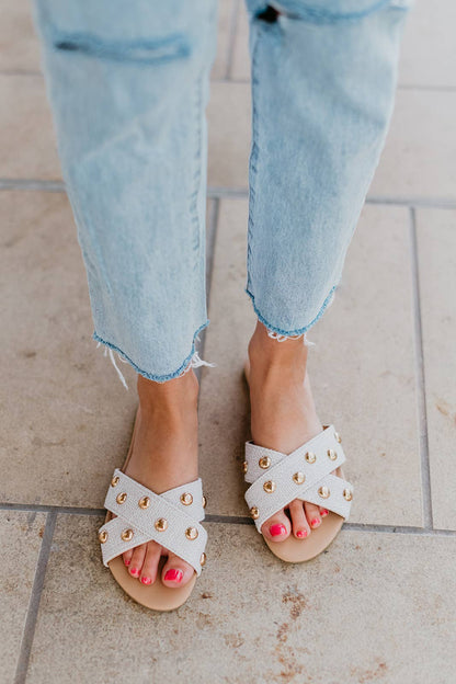 White sandals with gold accents worn with light blue jeans on a tiled floor.