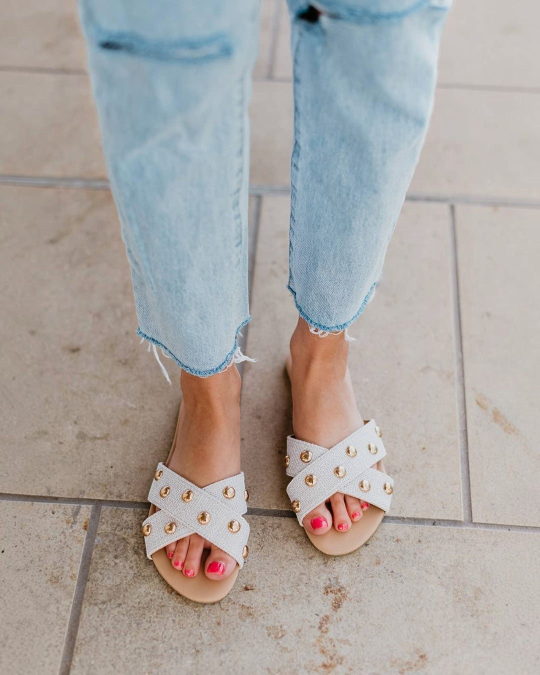 White sandals with gold accents worn with light blue jeans on a tiled floor.