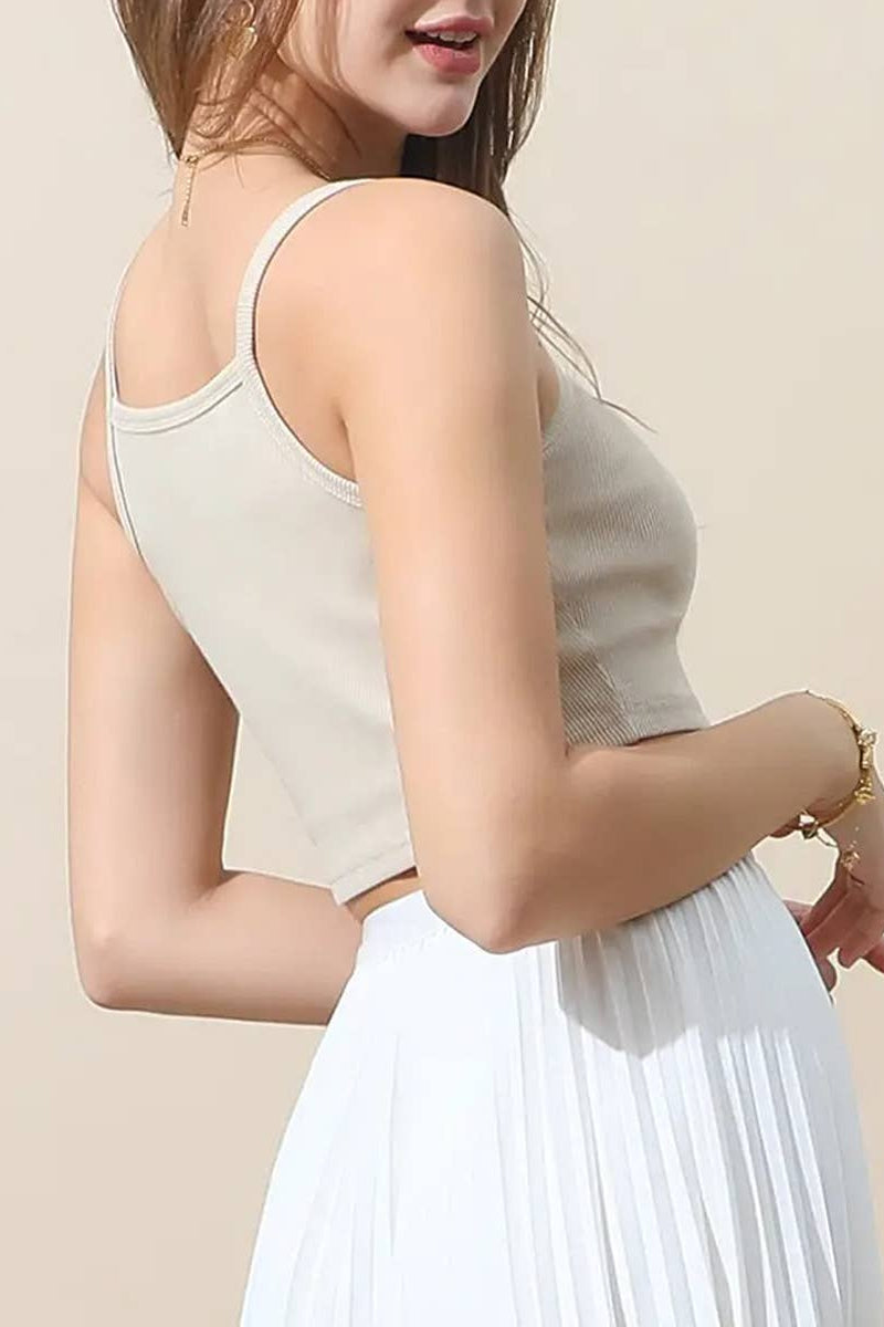 Woman wearing a beige sleeveless top and white pleated skirt on a plain background