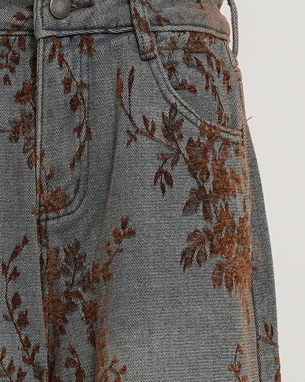 Close-up of a denim skirt with floral embroidery on a plain background