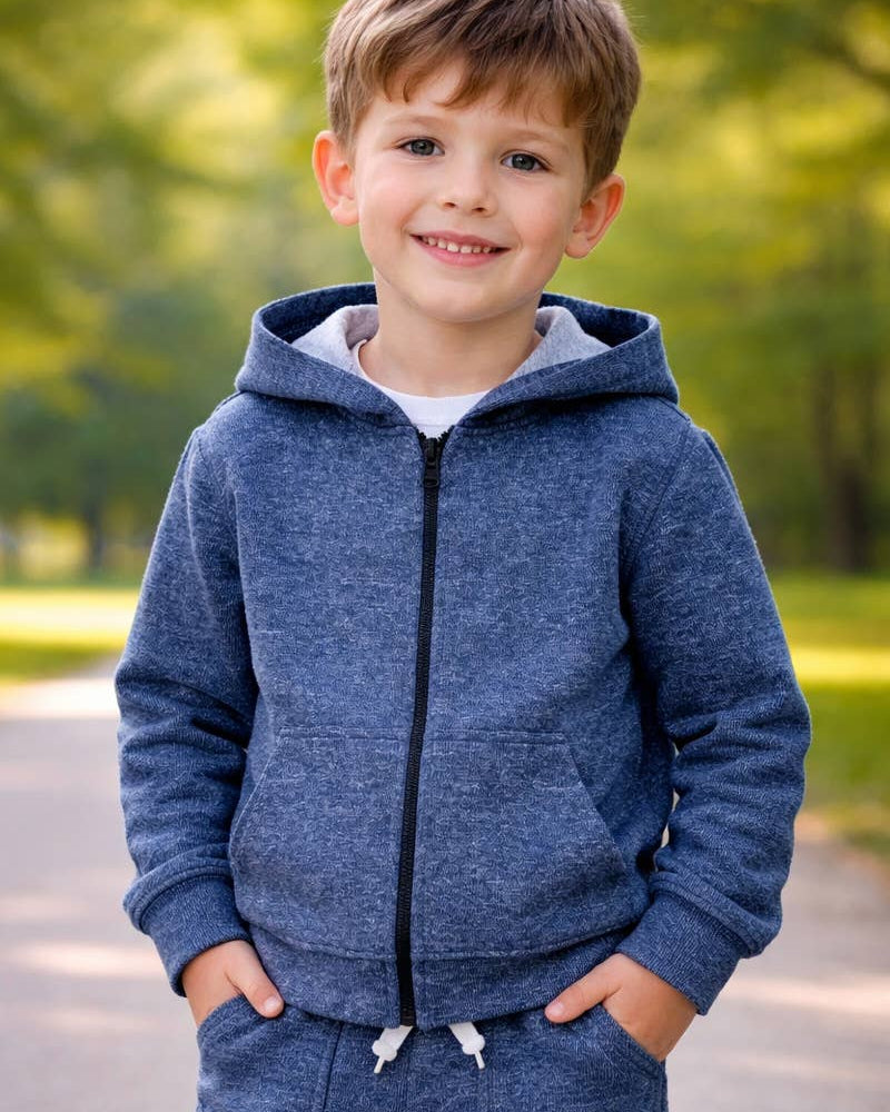 A young boy smiling outdoors, wearing a heathered blue zip-up hoodie with a black zipper and matching blue sweatpants.