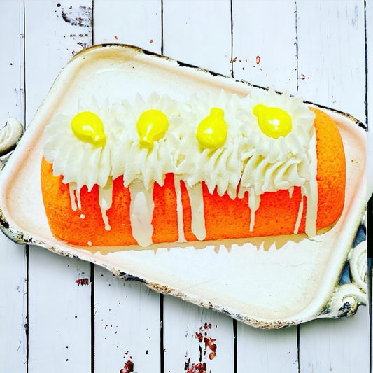 An orange twinkie bath bomb topped with white frosting and yellow sugar sprinkles on a white tray against a wood background