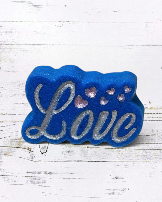 Calla Lily Cosmetics + CL kids blue heart-shaped Love bath bomb with silver glitter lettering on a bathroom counter