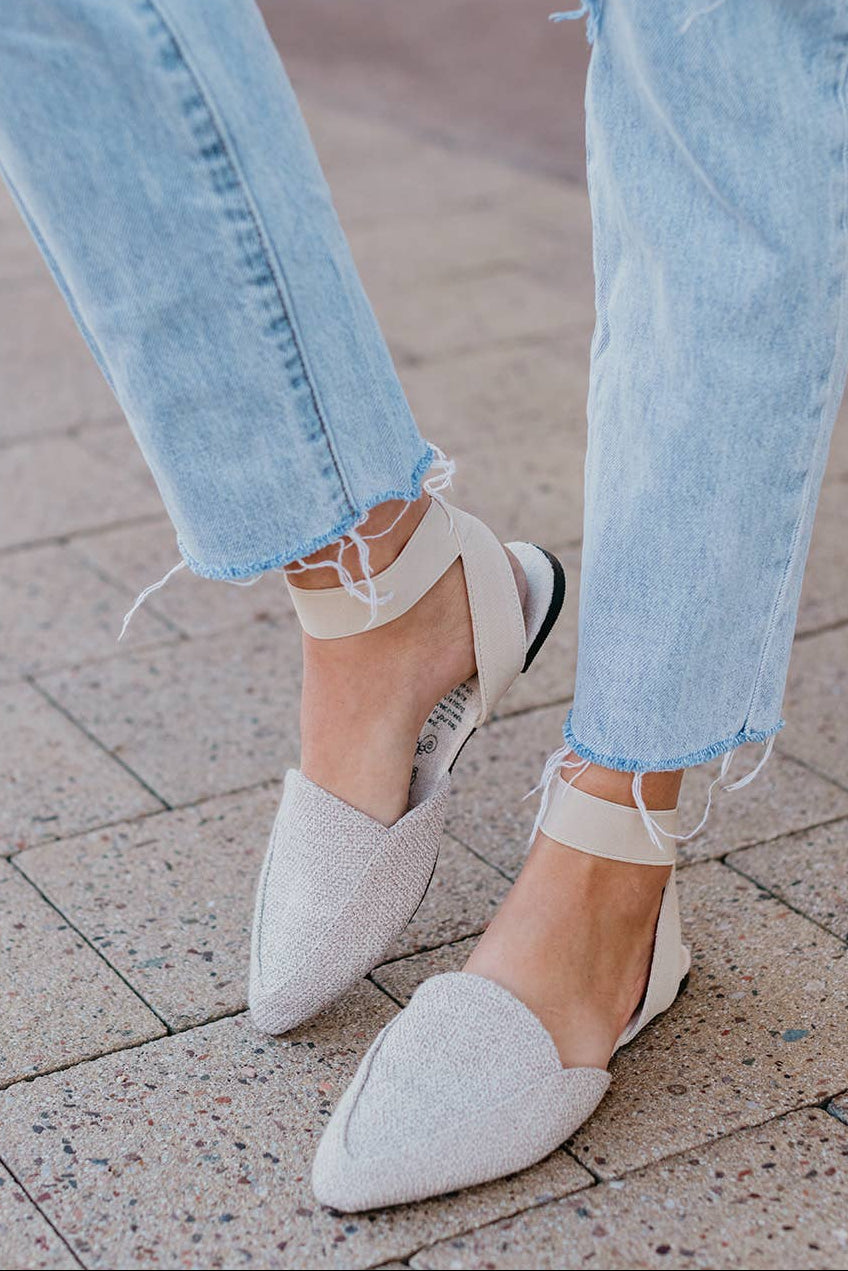 Close-up of light blue jeans and white pointed-toe shoes on a pavement.
