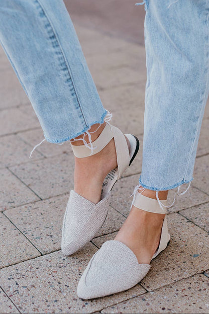 Close-up of light blue jeans and white pointed-toe shoes on a pavement.