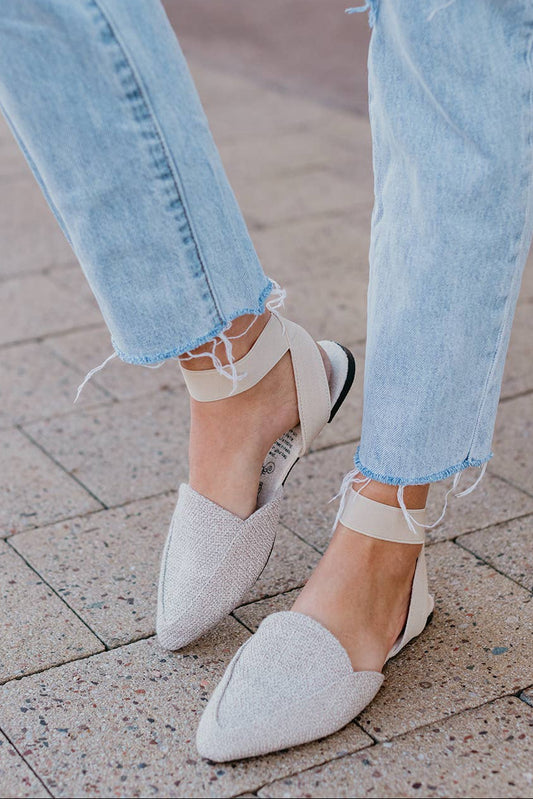 Close-up of light blue jeans and white pointed-toe shoes on a pavement.