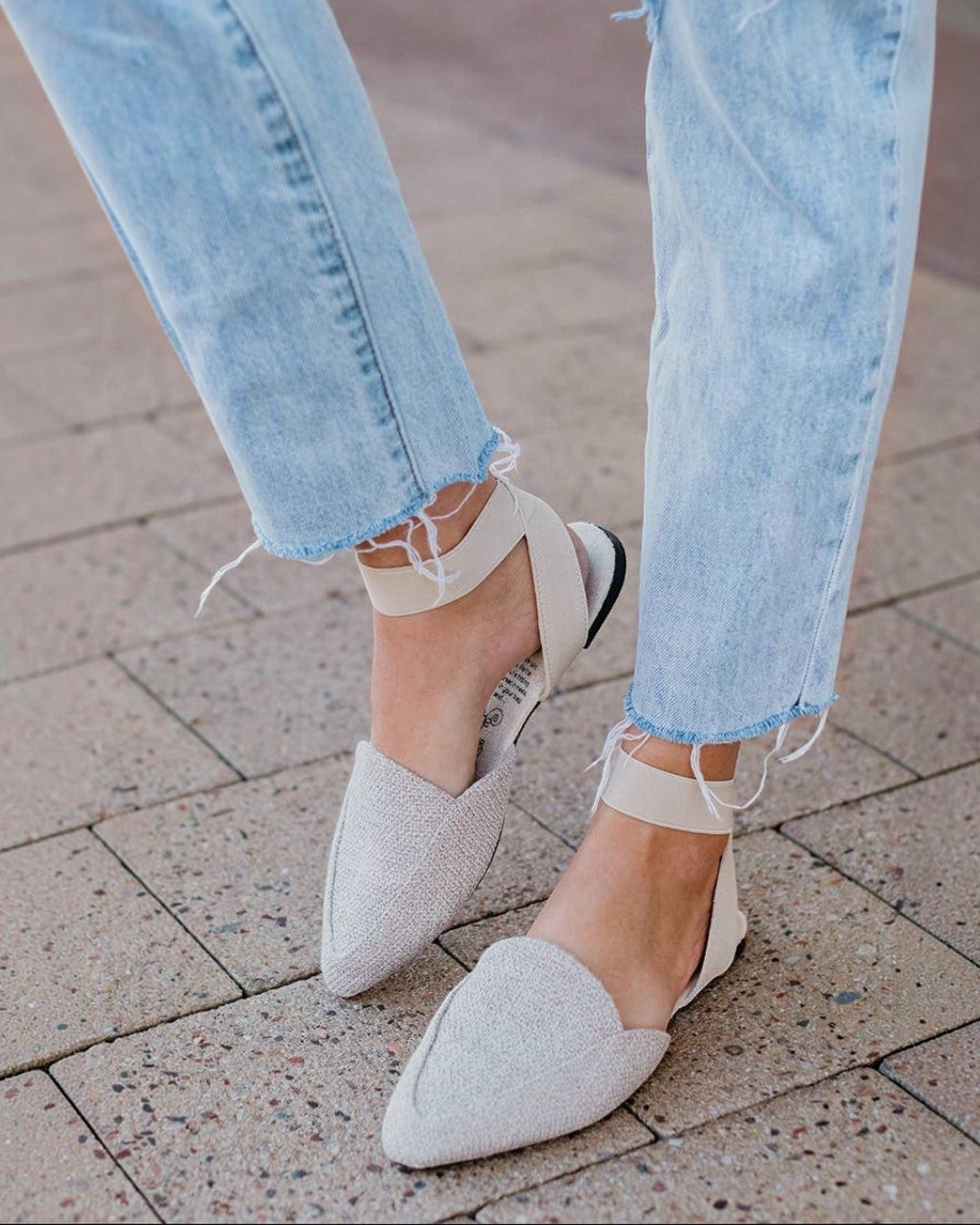 Close-up of light blue jeans and white pointed-toe shoes on a pavement.
