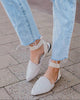 Close-up of light blue jeans and white pointed-toe shoes on a pavement.