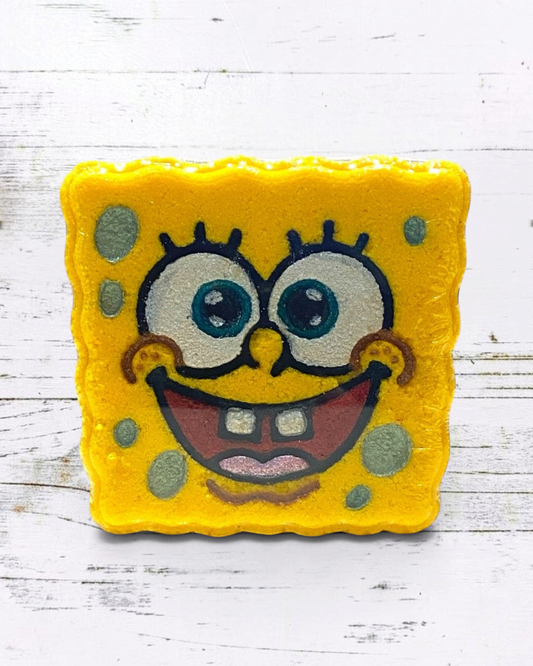 Calla Lily Cosmetics + CL kids Sponge Bob shaped yellow bath bomb with hand-painted details on a wood background