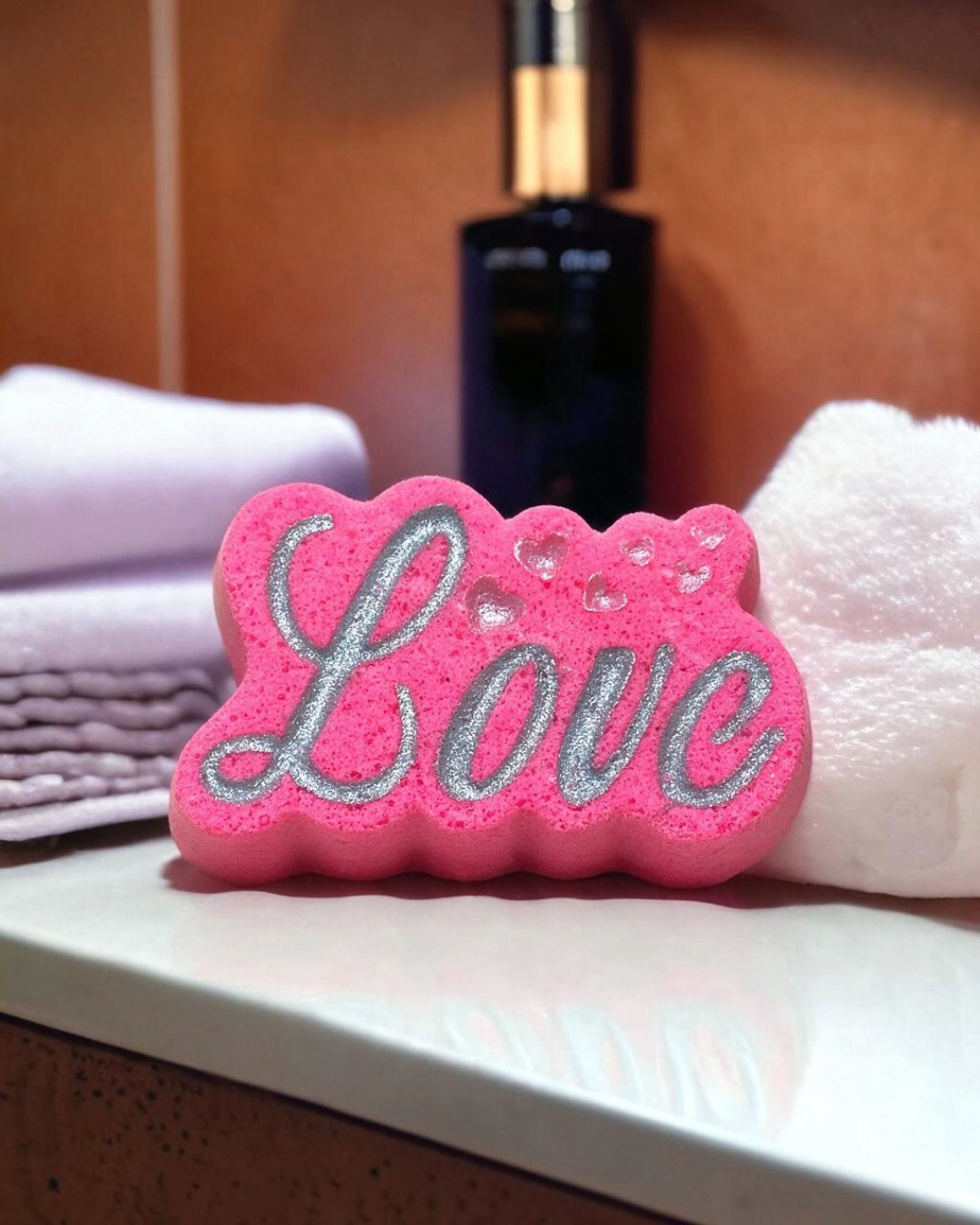 Calla Lily Cosmetics + CL kids pink Love bath bomb with silver glitter lettering and heart accents on a bathroom vanity