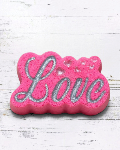 Calla Lily Cosmetics + CL kids pink Love bath bomb with silver glitter lettering and heart accents on a bathroom vanity