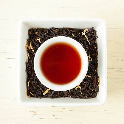 White bowl of black tea with tea leaves on a light wooden surface