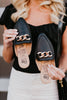 Black loafers with gold chain detail held by a person wearing a black top and white pants.
