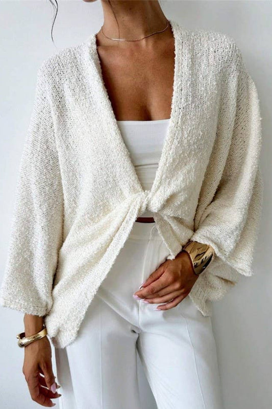 Person wearing a white textured cardigan over a white top and pants against a light background