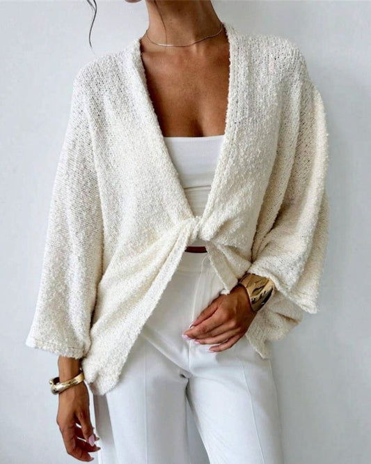 Person wearing a white textured cardigan over a white top and pants against a light background