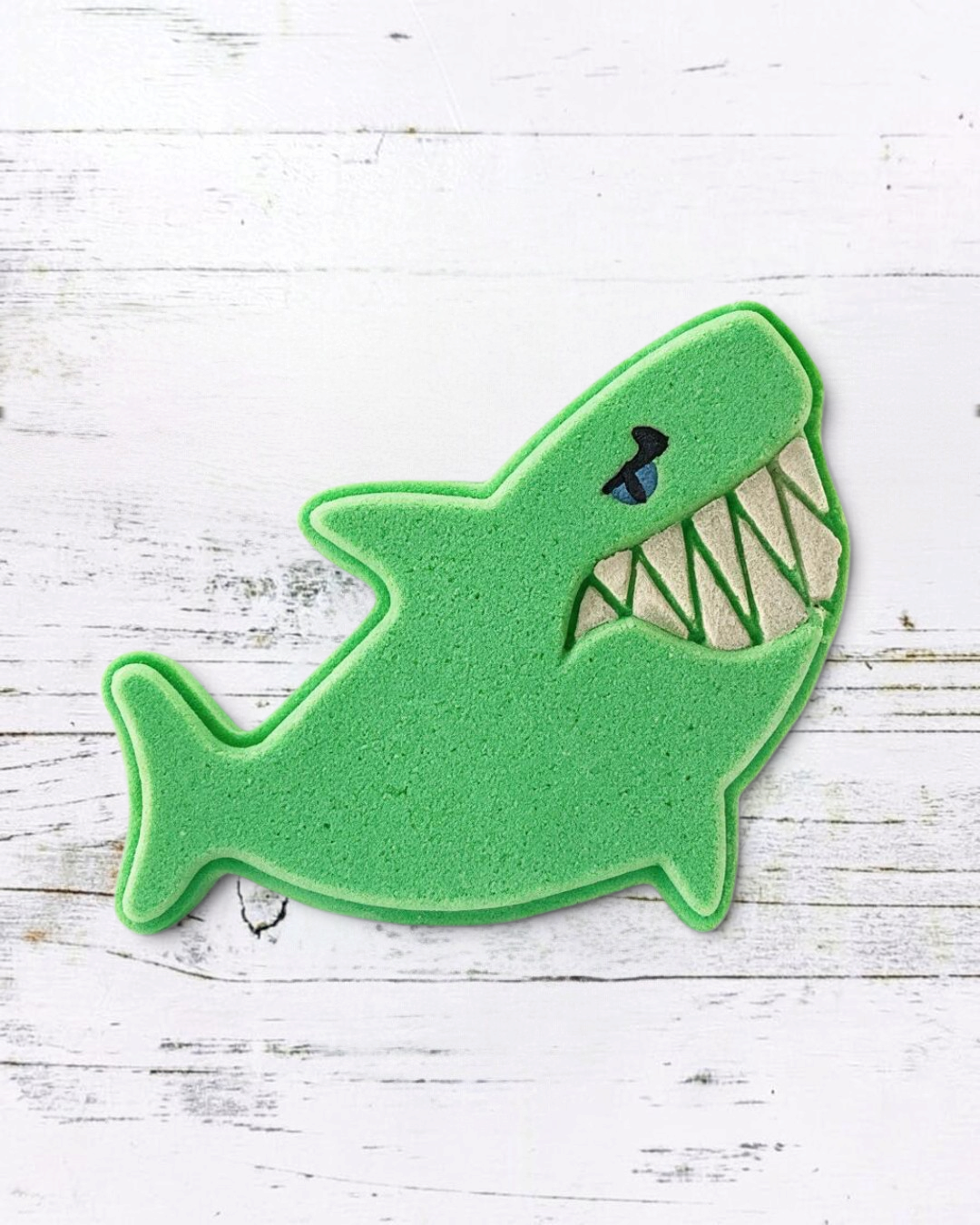 Calla Lily Cosmetics + CL kids green shark-shaped bath bomb with citrus scent on a white wooden background
