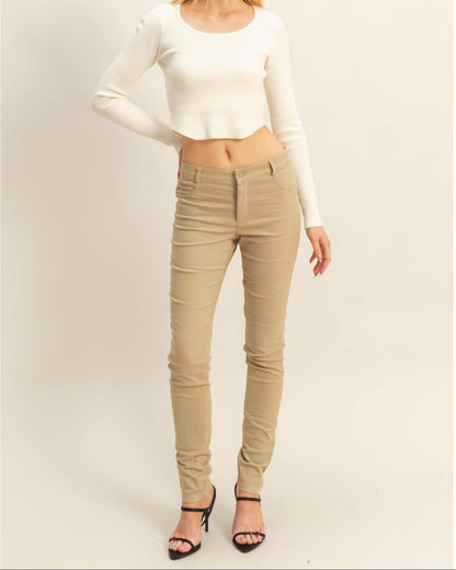 A woman modeling a fitted cream long-sleeve crop top and beige skinny jeans with black high-heeled sandals, standing against a plain light beige studio background.
