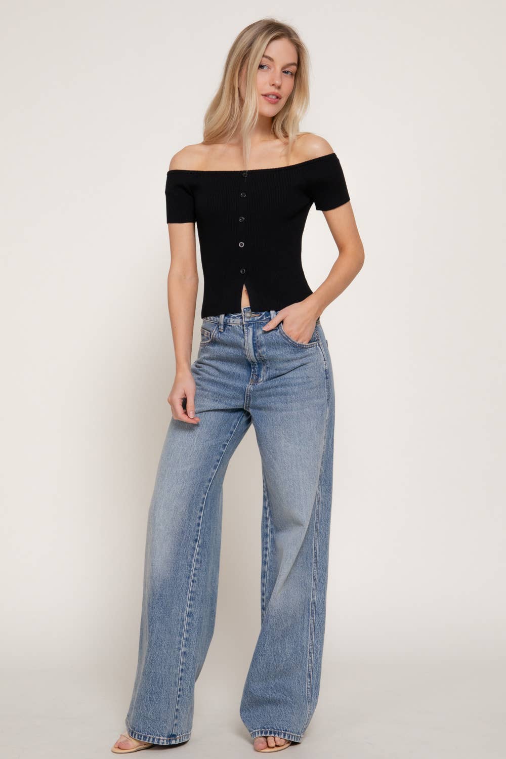 Woman wearing a black off-shoulder top and blue jeans on a plain background