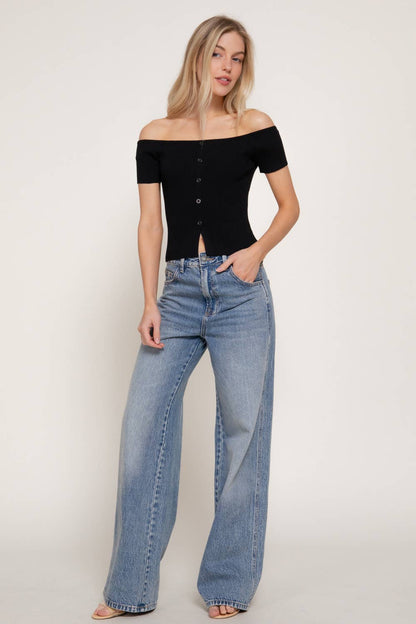Woman wearing a black off-shoulder top and blue jeans on a plain background