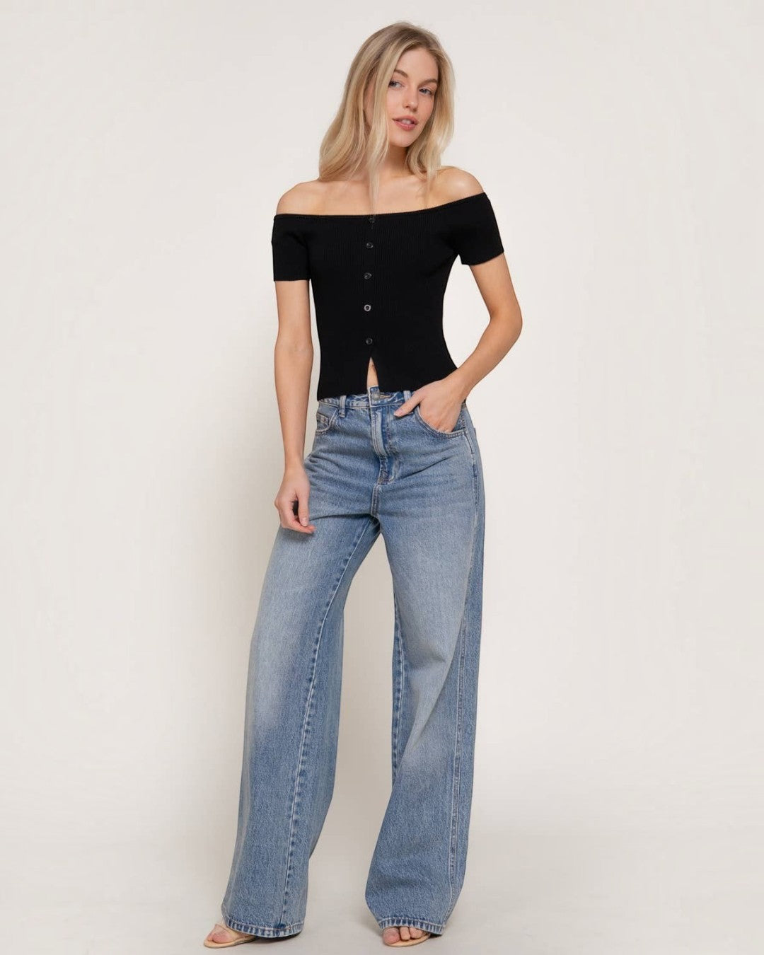 Woman wearing a black off-shoulder top and blue jeans on a plain background