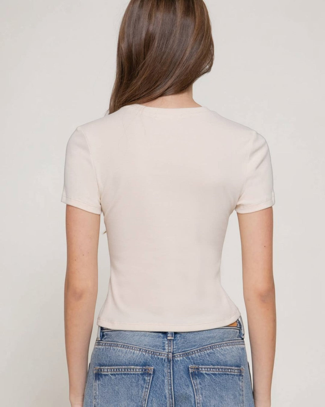 Person wearing a beige t-shirt and blue jeans against a plain background