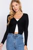 Woman wearing a black long-sleeve top over a white crop top and blue jeans on a light gray background
