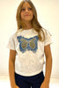 Young girl wearing a white t-shirt with a blue butterfly design on a plain background