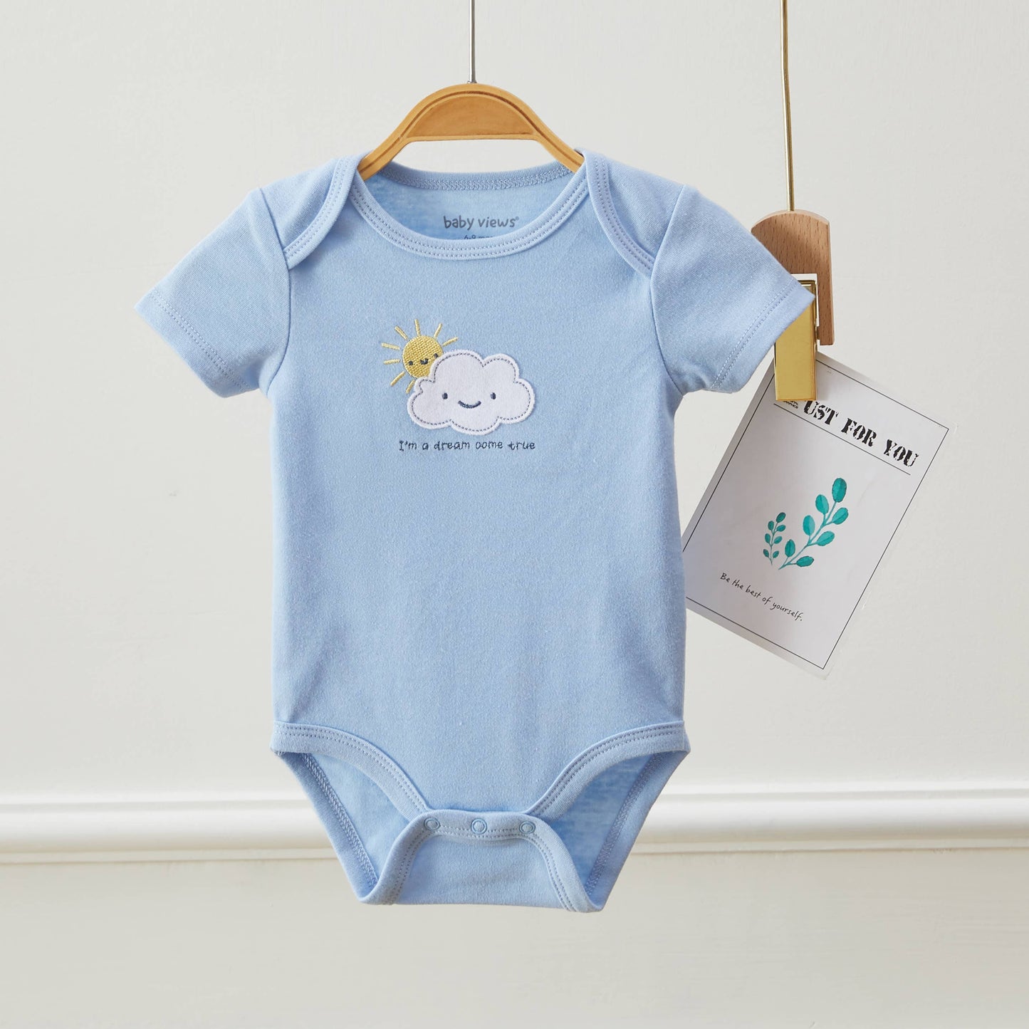 Light blue baby onesie with cloud and sun design on a hanger against a white background