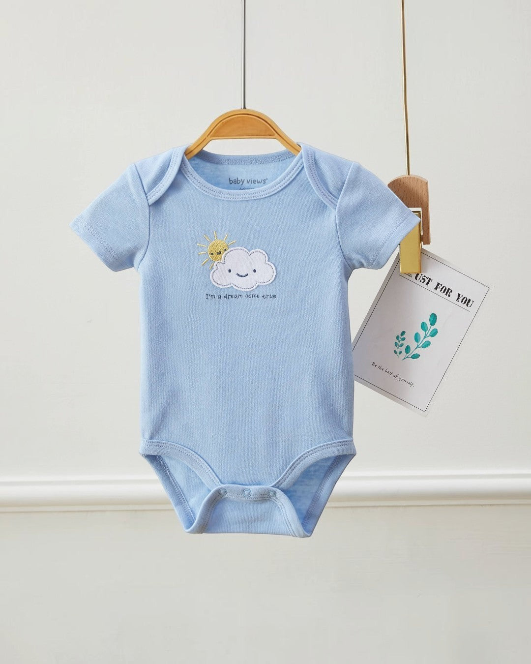 Light blue baby onesie with cloud and sun design on a hanger against a white background