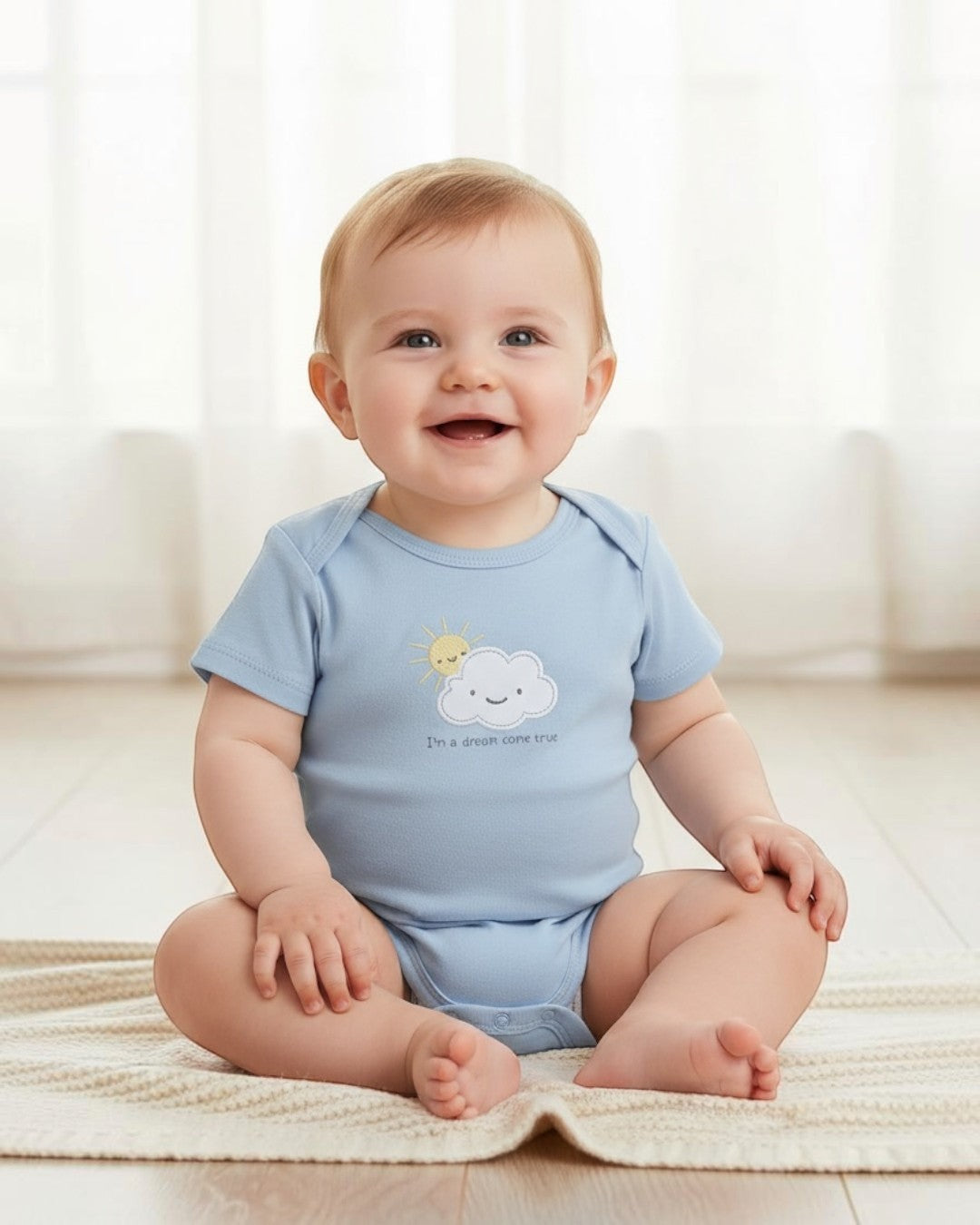 Baby wearing a light blue onesie with a cloud design, sitting on a beige blanket.