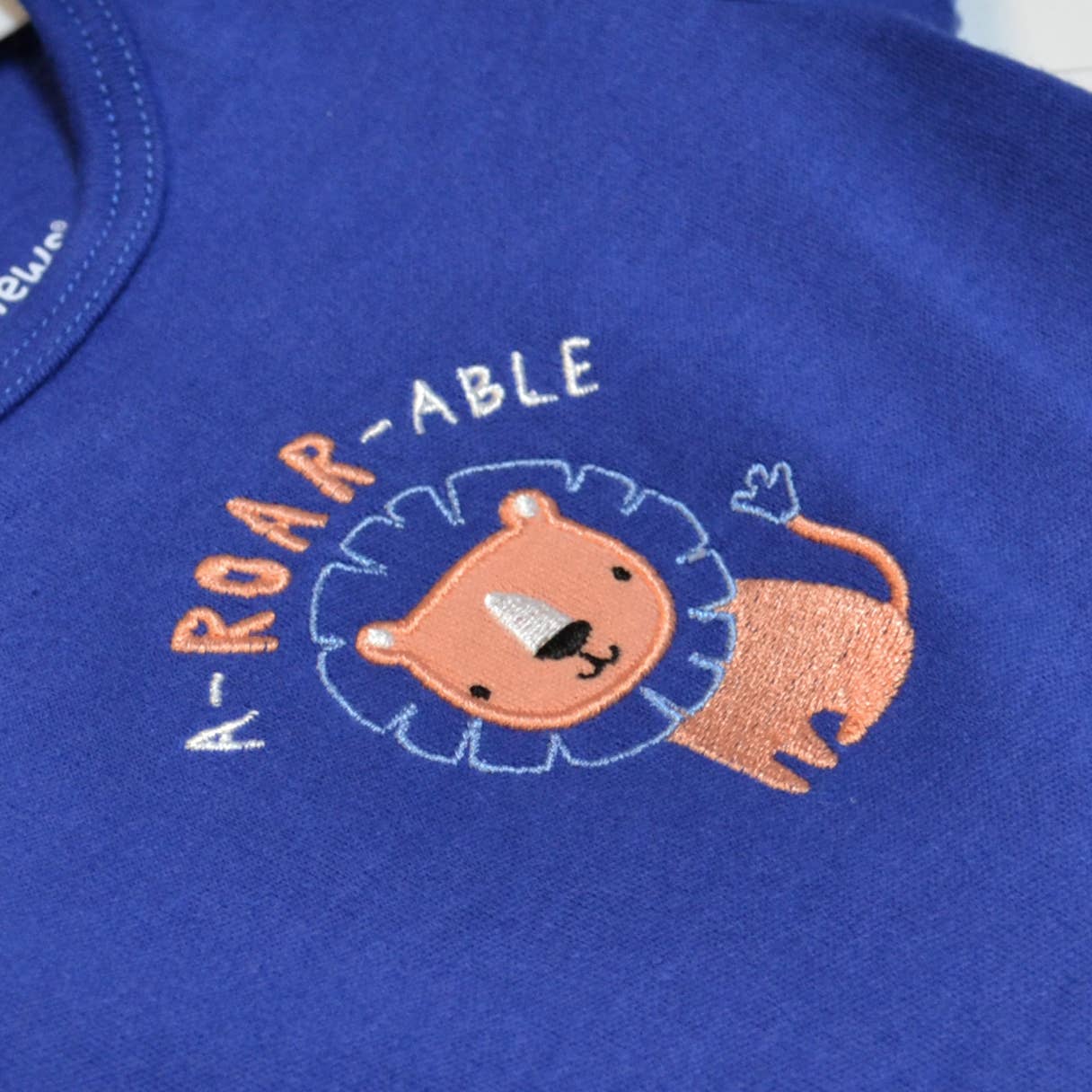 Embroidered lion design on a blue fabric with 'ROAR-ABLE' text.