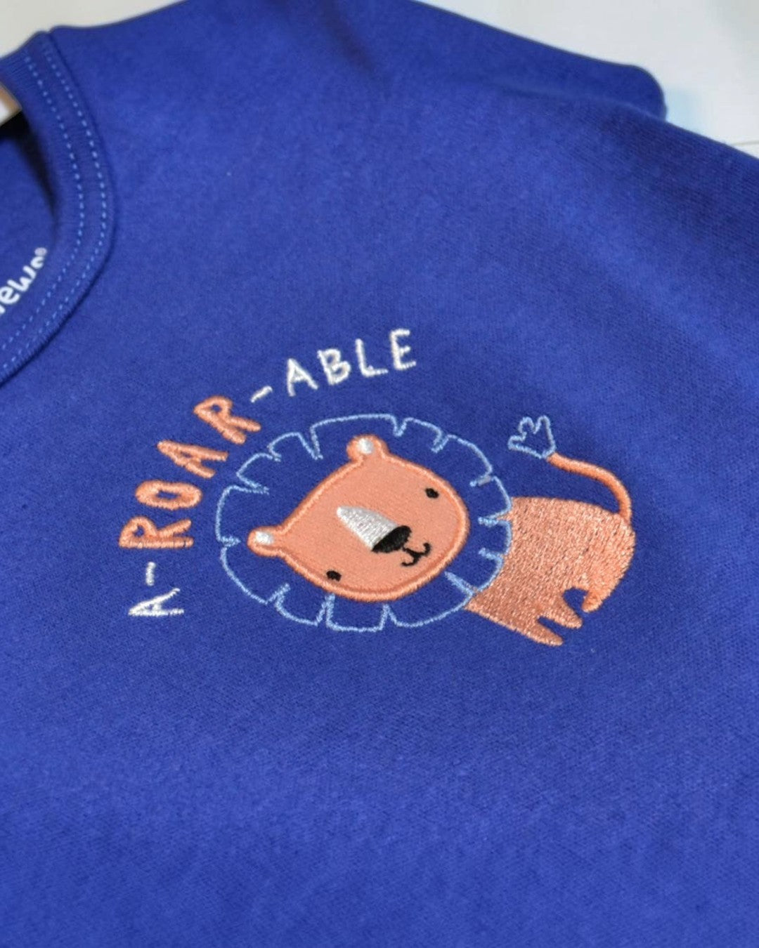 Embroidered lion design on a blue fabric with 'ROAR-ABLE' text.