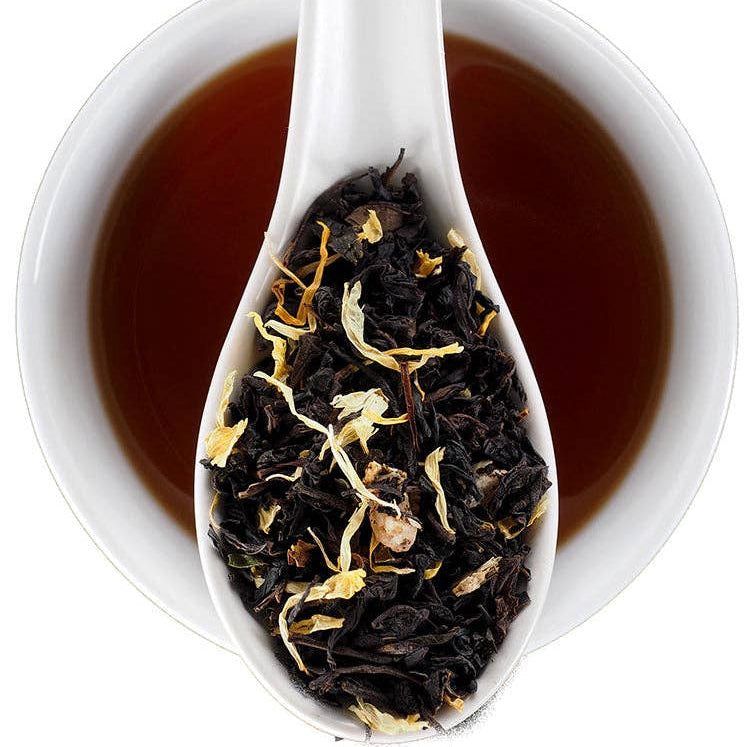 A white ceramic spoon resting over a white cup filled with dark amber tea, with loose-leaf tea and dried flower petals visible in the spoon. The Fine Elmwood Inn logo appears in the top right corner.