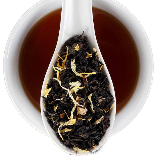 A white ceramic spoon resting over a white cup filled with dark amber tea, with loose-leaf tea and dried flower petals visible in the spoon. The Fine Elmwood Inn logo appears in the top right corner.