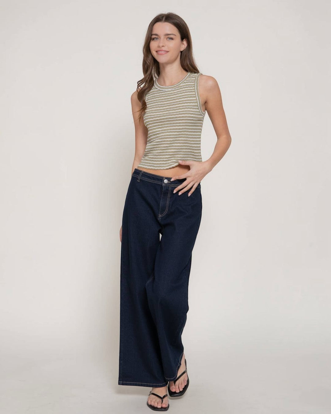 Woman wearing a striped tank top and wide-leg jeans on a plain background