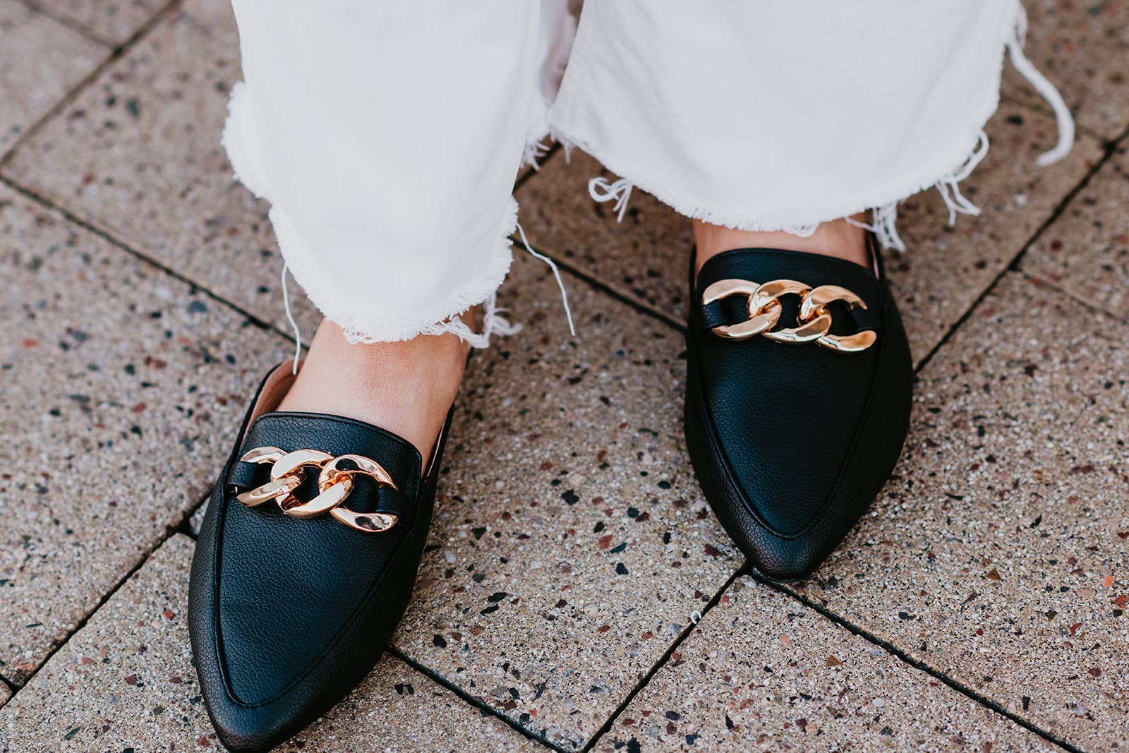 Black loafers with gold chain detail worn on a stone pavement