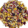 A circular pile of loose-leaf herbal tea blend featuring dried yellow chamomile flowers, purple rose petals, and small red berries on a solid white background.
