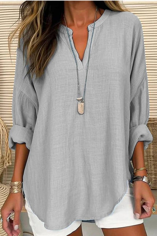 Woman wearing a gray oversized shirt with rolled-up sleeves and a necklace.
