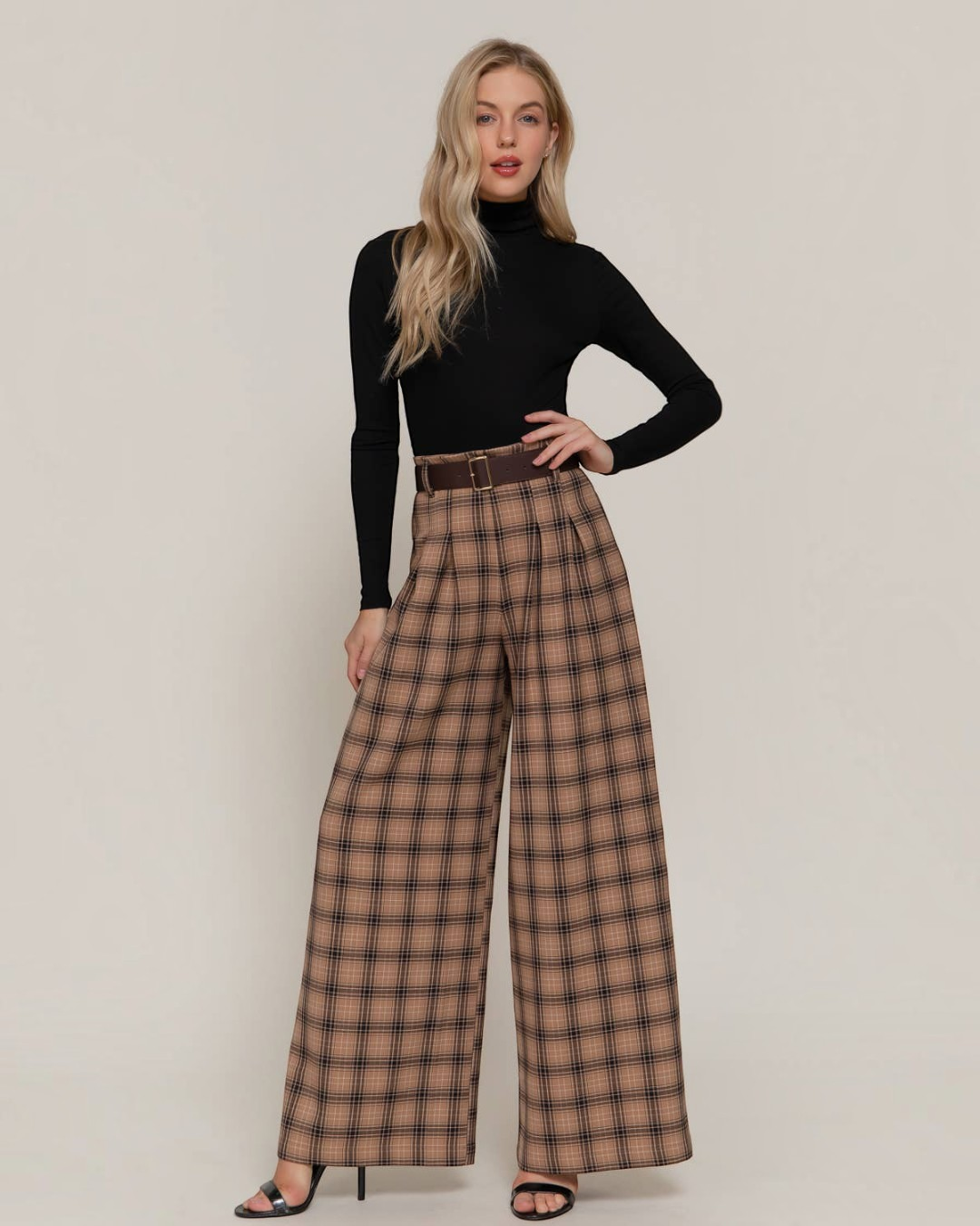 Model wearing Calla Lily Cosmetics + CL kids khaki plaid wide-leg pleated pants with a brown belt and black turtleneck.