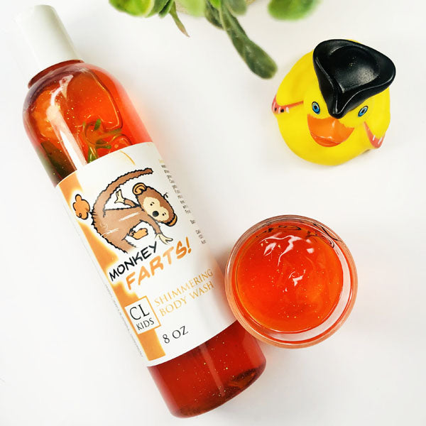 A transparent bottle and cup of our orange monkey farts body wash against a white background