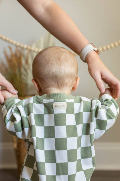Baby wearing a green and white checkered outfit with a blurred background