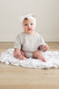 Baby sitting on a white blanket wearing a light gray outfit and white headband.
