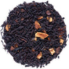 A circular pile of loose-leaf tea blend on a plain white background. The tea consists of very dark brown to near-black dried leaves with scattered light tan dried fruit pieces.
