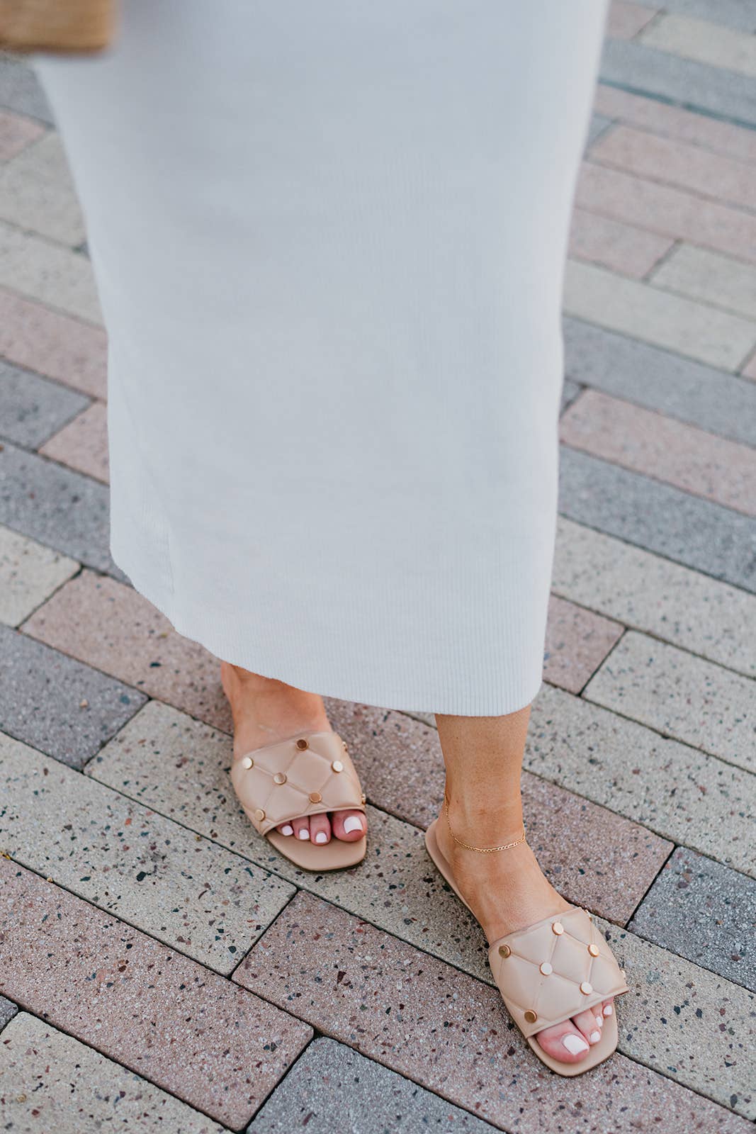 Person wearing white pants and beige sandals on a brick pavement
