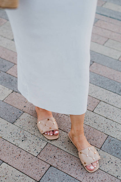 Person wearing white pants and beige sandals on a brick pavement