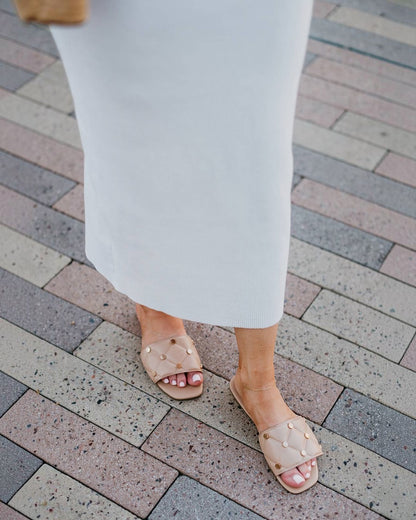 Person wearing white pants and beige sandals on a brick pavement