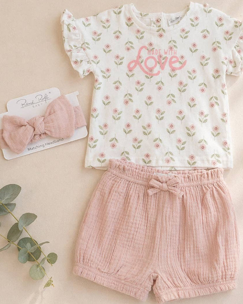 Baby outfit with floral top and pink shorts on a beige background