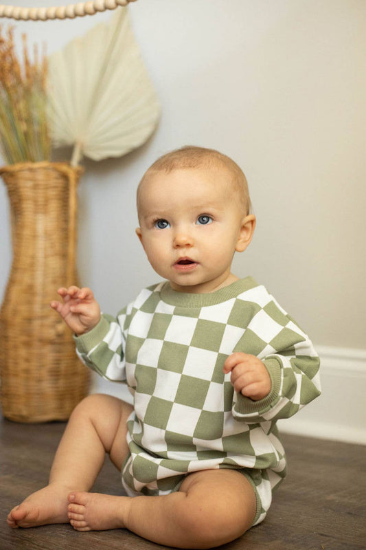 Baby wearing a green and white checkered outfit sitting on the floor.