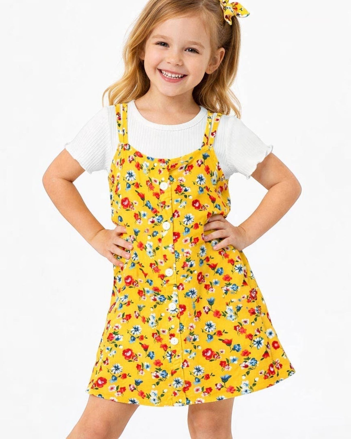 Young girl wearing a yellow floral pinafore dress with a white shirt underneath on a white background